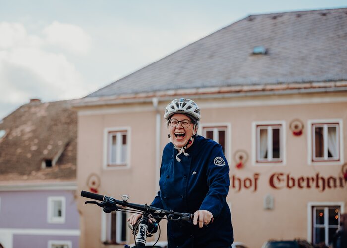 Frau neben Fahrrad lacht in die Kamera vor dem Gasthof Eberhard