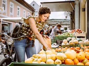 Frau greift sich am Bauernmarkt in Leoben eine Mandarine bei einem Stand mit Menschen drum herum