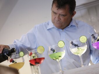 Ein Mann, der eine Reihe bunter Cocktails verziert.