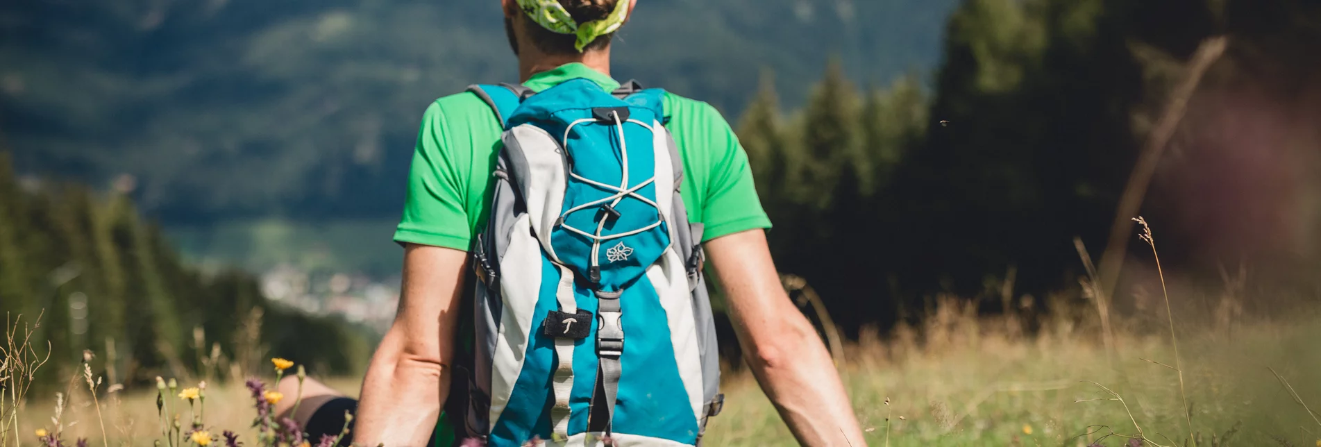 Ein Wanderer sitzt auf einer Wiese und blickt in die Ferne