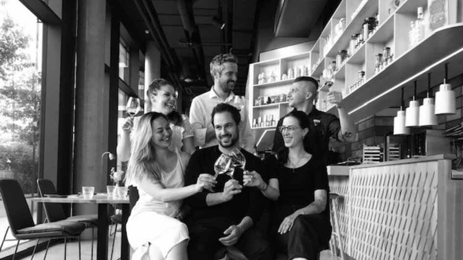 Gruppe von sechs Personen hebt Gläser in einer modernen Bar.