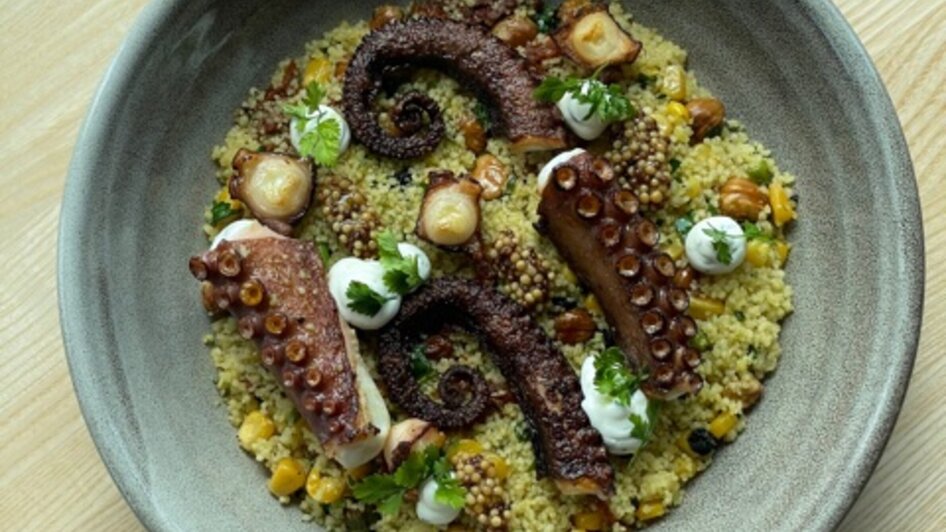Ein Teller mit gegrilltem Octopus auf Couscous mit Gemüse.