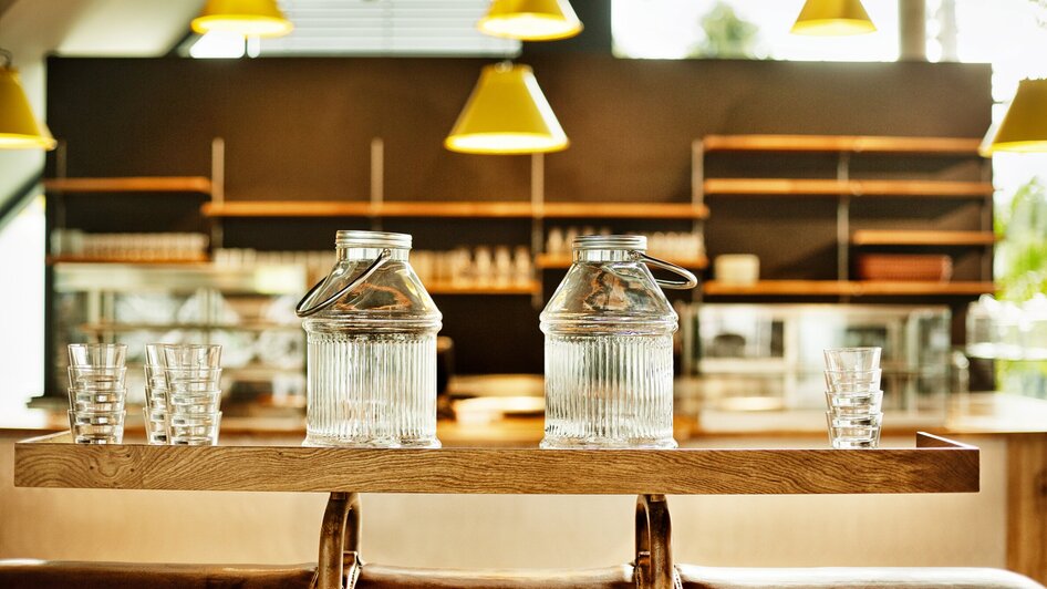 Zwei Glaskaraffen mit Gläsern auf einem Holztablett in einem Café.