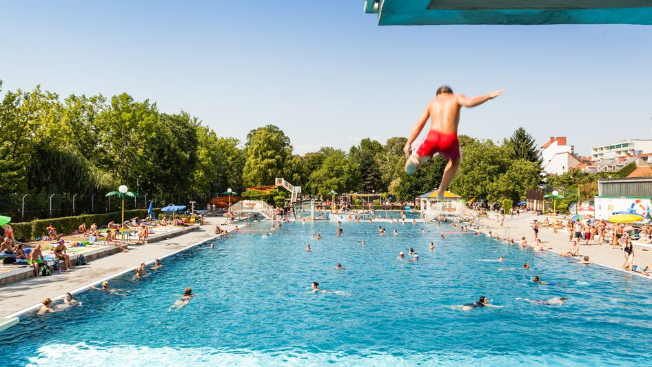 Ein Junge springt ins Schwimmbecken des Augartenbads in Graz an einem sonnigen Tag. | © Holding Graz - Joel Kernasenko