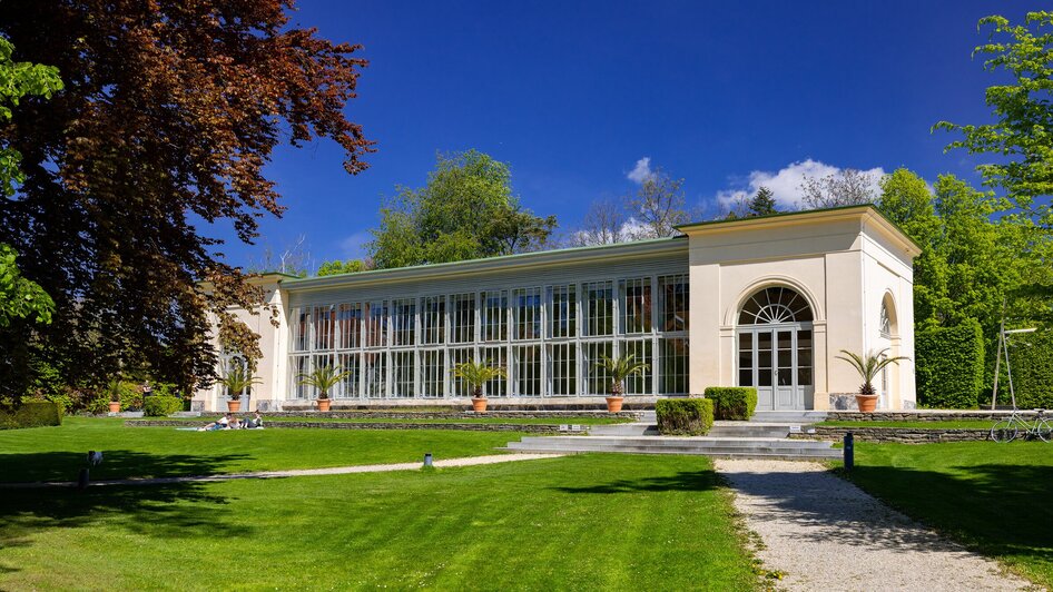 Ein Glashaus im Burggarten in Graz, umgeben von Grün und blauem Himmel. | © Graz Tourismus - Harry Schiffer