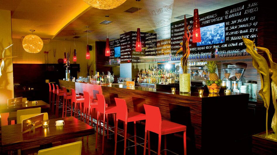 Moderne Bar mit farbigen Stühlen und beleuchteter Theke. | © Cafe Glockenspiel