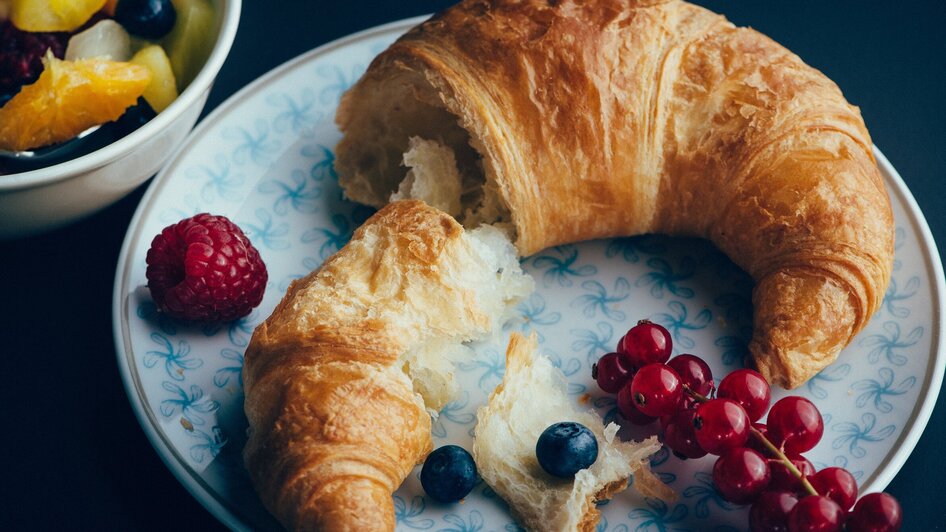 Ein frischer Croissant auf einem Teller mit Beeren und Obstsalat.