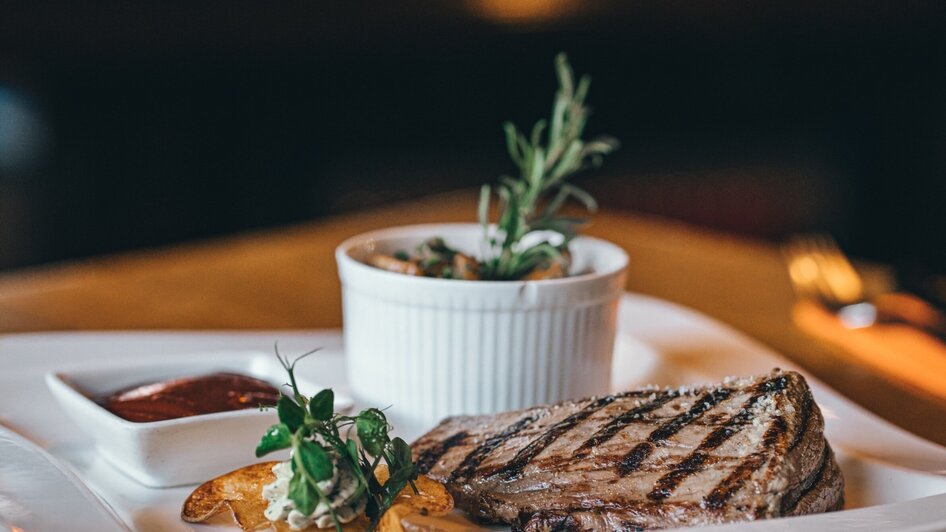Gegrilltes Steak mit Saucen und Beilagen serviert auf einem weißen Teller.