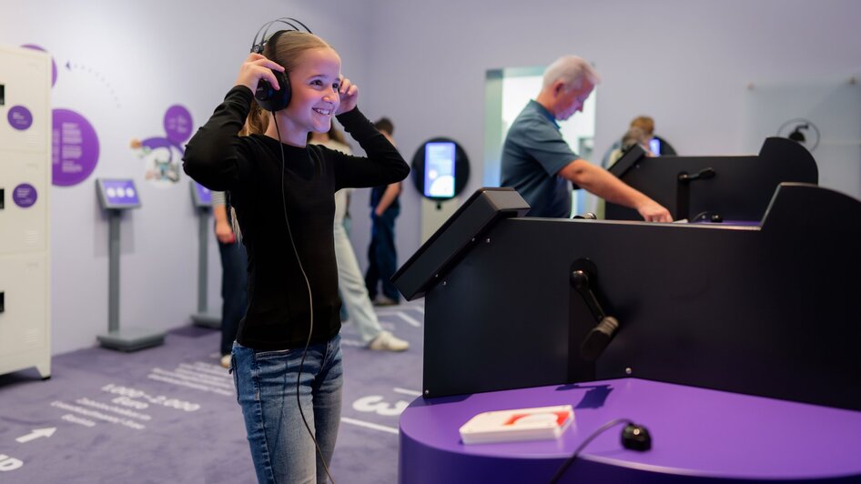 Ein lächelnder Teenager trägt Kopfhörer und erkundet interaktive Displays im Museum.