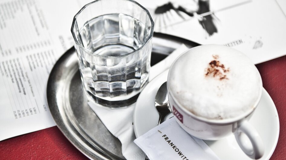 Eine Tasse Cappuccino und ein Glas Wasser auf einem Tablett.