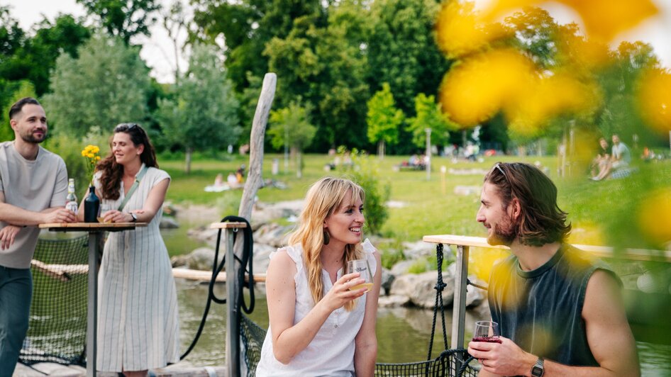 Entspannte Zeit mit Freunden am Wasser mit Getränken und Blumen. | © Graz Tourismus - Mias Photoart