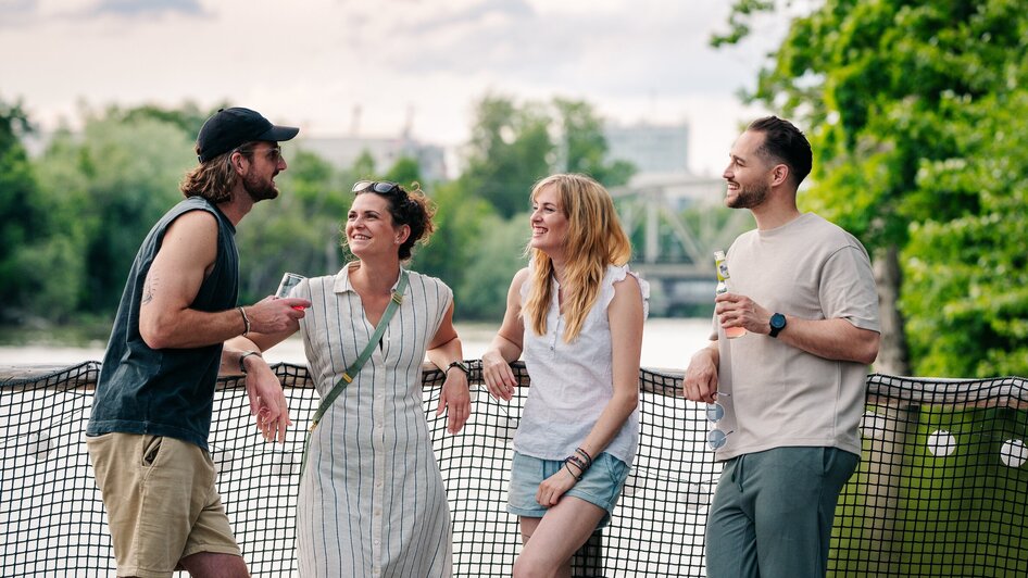 Vier Freunde stehen auf einem Floß auf der Mur und unterhalten sich. | © Graz Tourismus - Mias Photoart