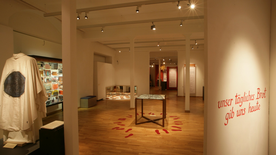 Innenansicht einer Ausstellung mit Fußspuren und dem Text: 'unser tägl. Brot gib uns heute'. | © Diözesanmuseum Graz