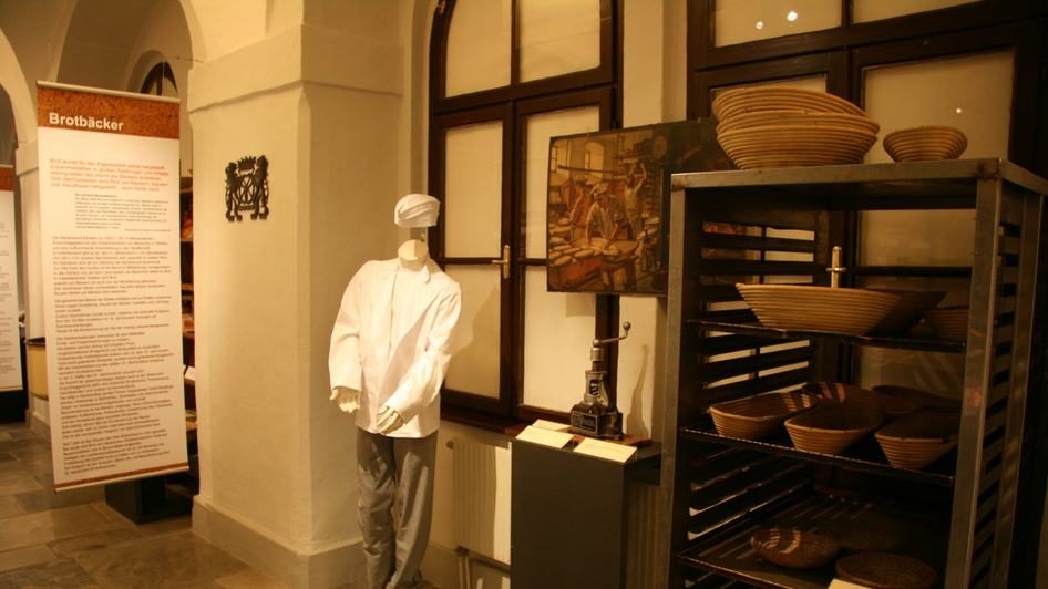 Eine Ausstellung mit einer Schaufensterpuppe in Bäckerkleidung, historischen Backwerkzeugen und Brotformen. | © Diözesanmuseum Graz