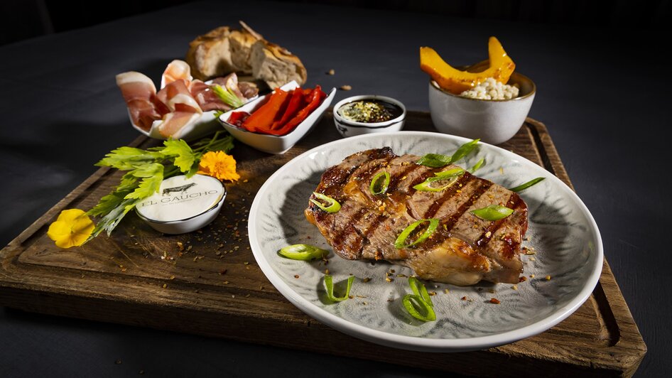 Gegrilltes Steak mit Beilagen auf einer Holzplatte.