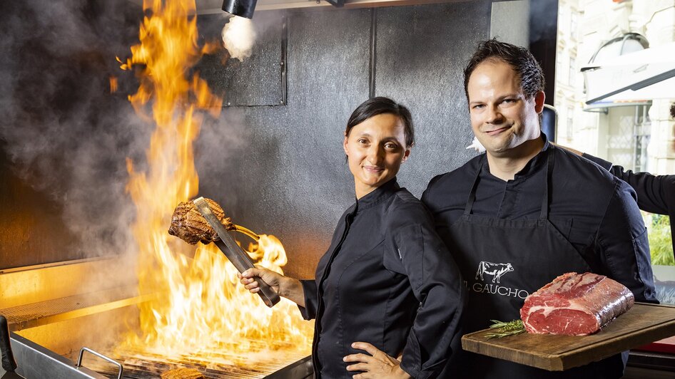 Köche am Grill mit Flammen und frischem Fleisch in Graz.