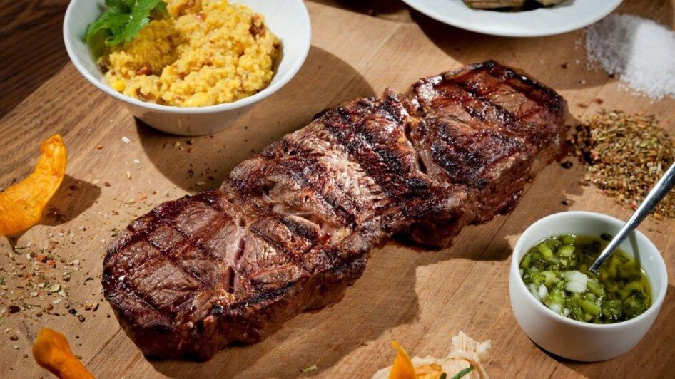 Saftiges Steak auf Holzbrett, begleitet von Beilagen.