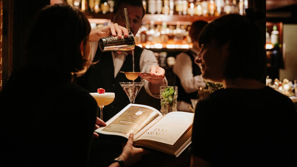 Zwei Gäste in der Bar, während ein Barkeeper Cocktails zubereitet. | © Daniel Kindler