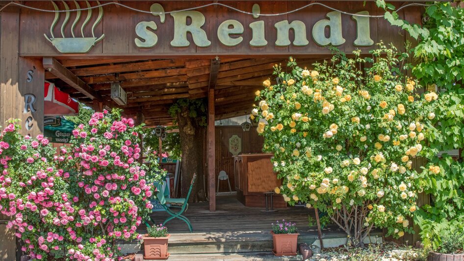 Die Eingangstür des Gasthofs s'Reindl, umgeben von blühenden Pflanzen. | © sReindl