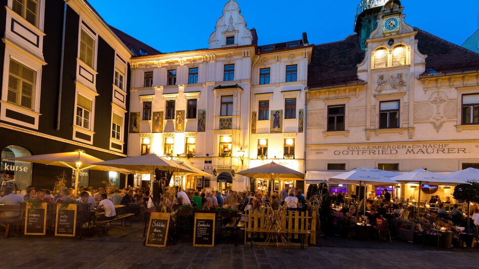 Belebter Glockenspielplatz mit Restaurants und beleuchtetem Glockenspiel.