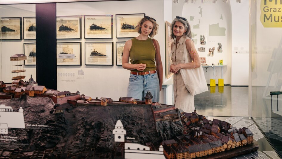 Zwei Frauen betrachten ein detailliertes Stadtmodell von Graz im Museum. | © Graz Tourismus - Mias Photoart