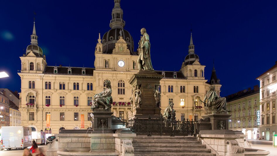 Abendliche Ansicht des Rathauses am Hauptplatz in Graz mit Statuen und historischem Hintergrund. | © Graz Tourismus - Harry Schiffer