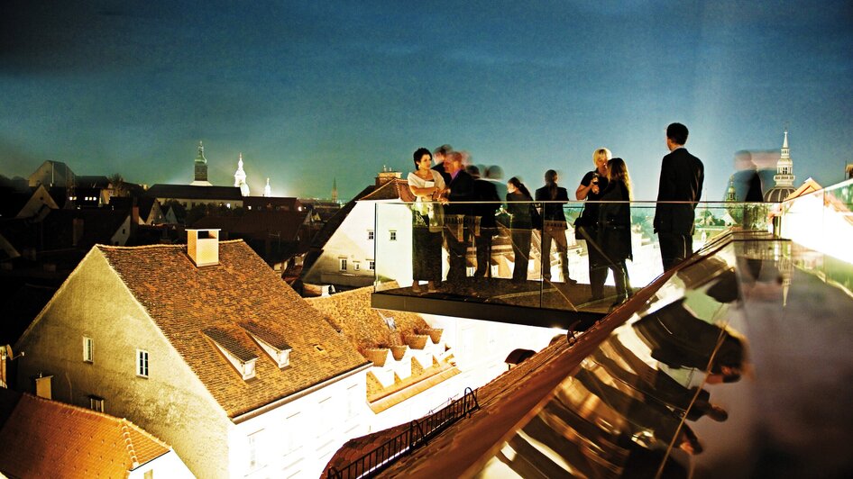 Networking auf einer modernen Terrasse in Graz bei Nacht.