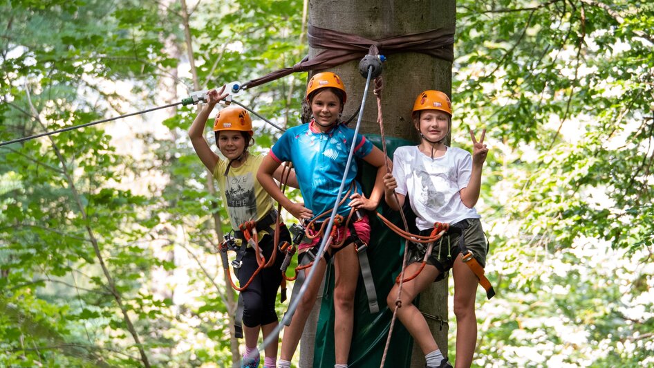 Drei Kinder im Kletterwald mit Sicherheitsausrüstung und Helmen.