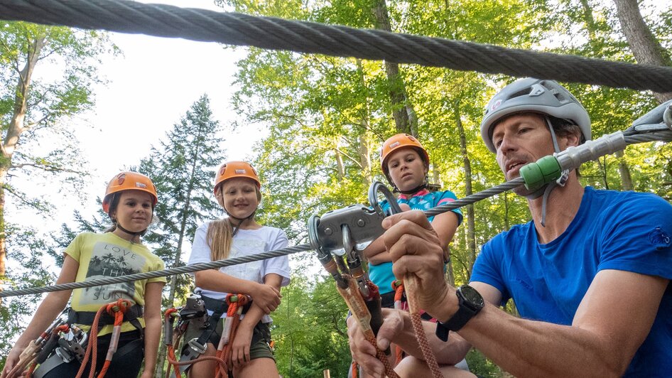 Eine Gruppe von Kindern mit Helmen beobachtet einen Klettertrainer.