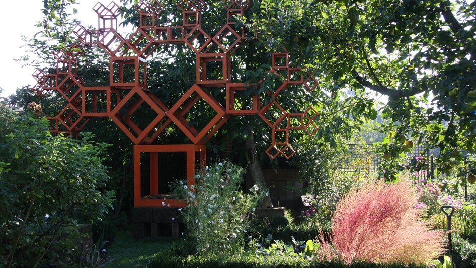 Ein kreativer Garten mit einem auffälligen, orangefarbenen Baumdesign aus geometrischen Formen. | © kunstGarten