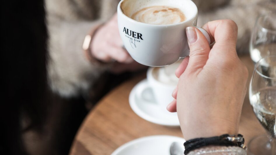 Eine Hand hält eine Tasse Kaffee mit Milchschaum in der Bäckerei Martin AUER.