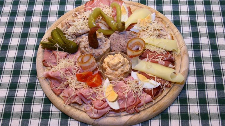 Ein Holzbrett mit verschiedenen Wurst- und Käseaufschnitten sowie Beilagen.