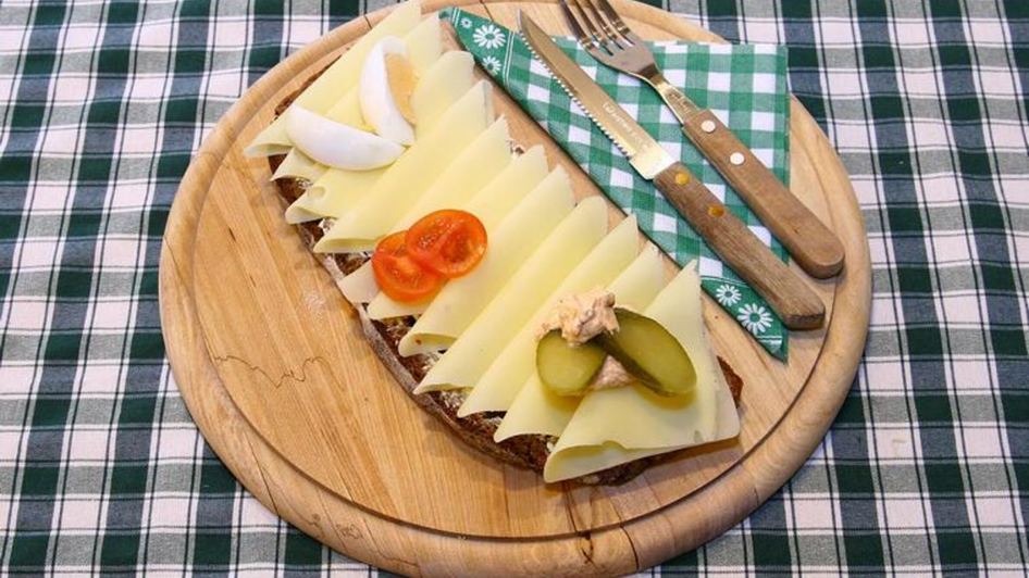 Ein Holzbrett mit einem Käsebrot, garniert mit Gurken, Ei und Tomaten.