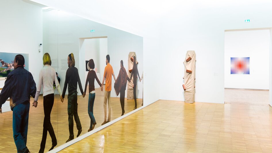 Einblicke in eine Kunstgalerie mit reflektierenden Figuren.