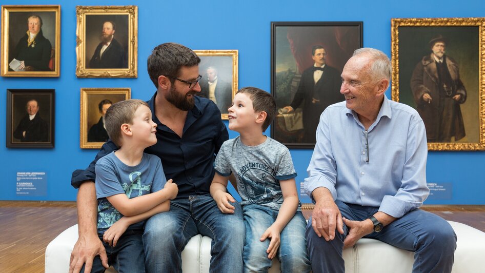 Vater, Großvater und zwei Kinder sitzen zusammen in der Galerie.