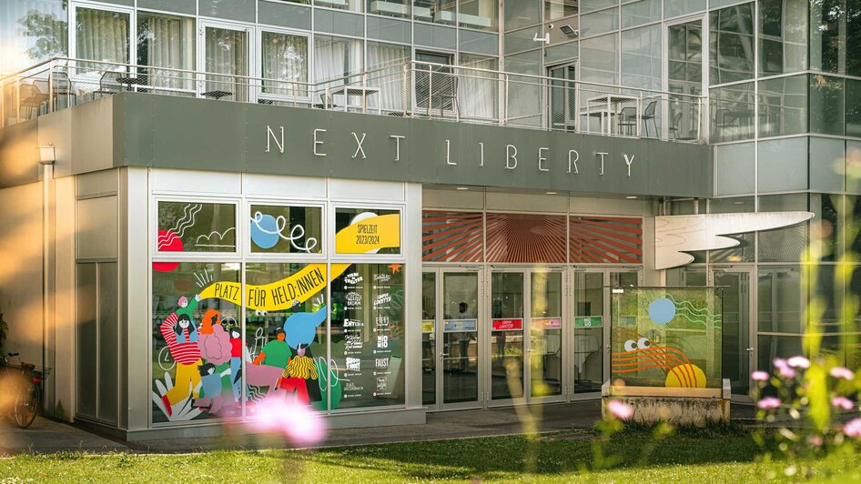 Das Next Liberty präsentiert moderne Architektur mit großen Fenstern und bunten Grafiken. Der Veranstaltungsort bietet eine helle Atmosphäre für Konferenzen und Networking.