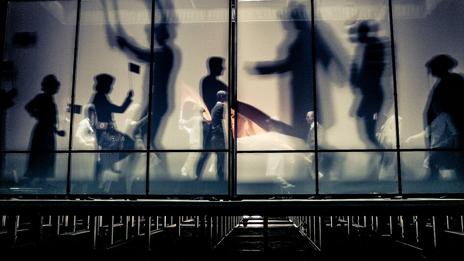 Menschen bewegen sich im Next Liberty, moderne Architektur mit großflächigen Fenstern und einem offenen Raumgefühl. Die Lichtverhältnisse schaffen eine dynamische Atmosphäre für Konferenzen und Networking.