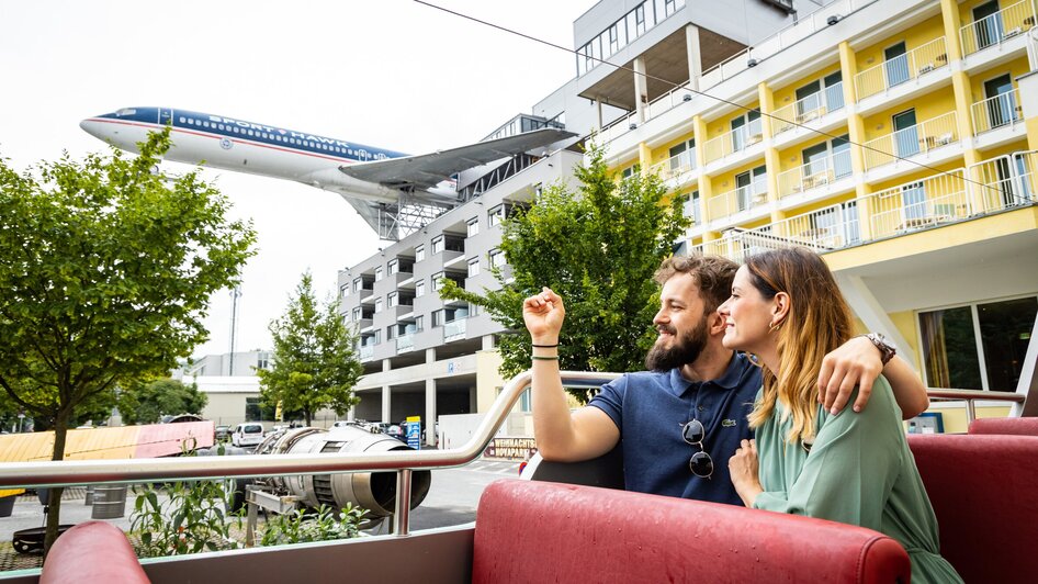 Paar genießt die Aussicht bei einer kulinarischen Tour mit dem Cabriobus - im Hintergrund ein Flugzeug des Flugzeug-Restaurants NOVAPARK.