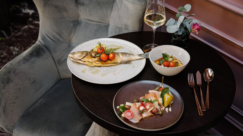 Ein gedeckter Tisch im Operncafé mit gebratenem Fisch, Salat und einem Glas Weißwein.
