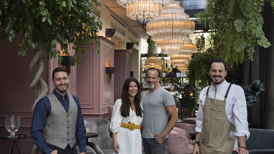 Vier Personen posieren in einem stilvollen Restaurant mit großen Kronleuchtern.