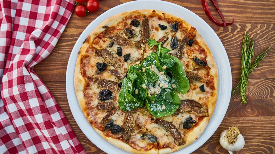 Leckere Pizza mit Spinat, Oliven und getrockneten Tomaten auf einem Holzuntergrund. | © Pixabay