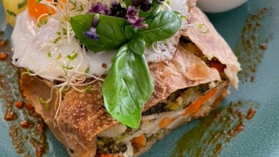 Vegetarischer Gemüse-Strudel mit Spiegelei, Beilagen und Kräutern auf einem Teller. | © PEP