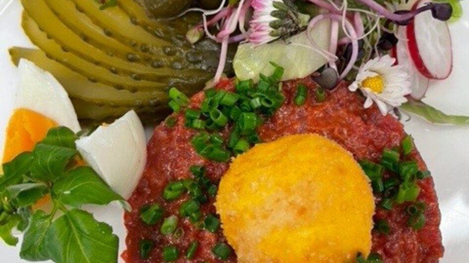 Detailansicht eines kulinarischen Gerichts mit Beef Tartar und Beilagen wie Gurken und Kräuter. | © PEP