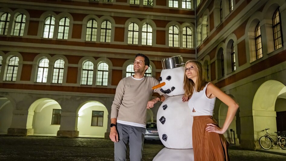Paar mit einem Schneemann im Innenhof des Priesterseminars bei einem geführten Abend-Rundgang in Graz. | © Graz Tourismus - Werner Krug
