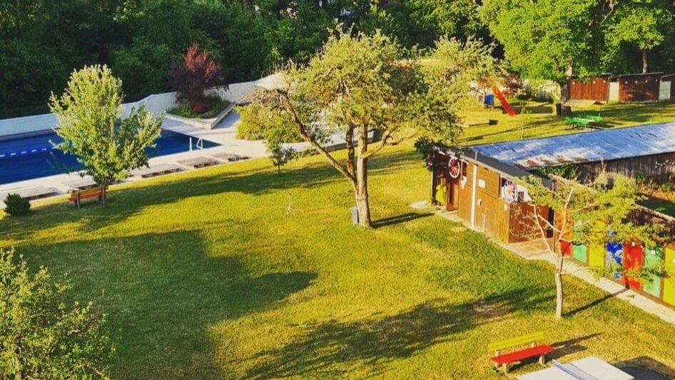 Grüne Wiese mit Picknicktischen und Schwimmbad im Hintergrund. | © Ragnitzbad