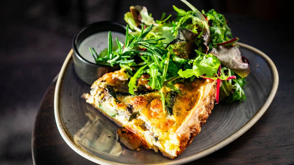 Ein Stück Quiche mit frischem Salat und Dressing auf einem Teller.