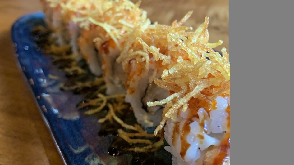 Leckeres Sushi mit knusprigem Belag auf einem Teller in einem Restaurant.