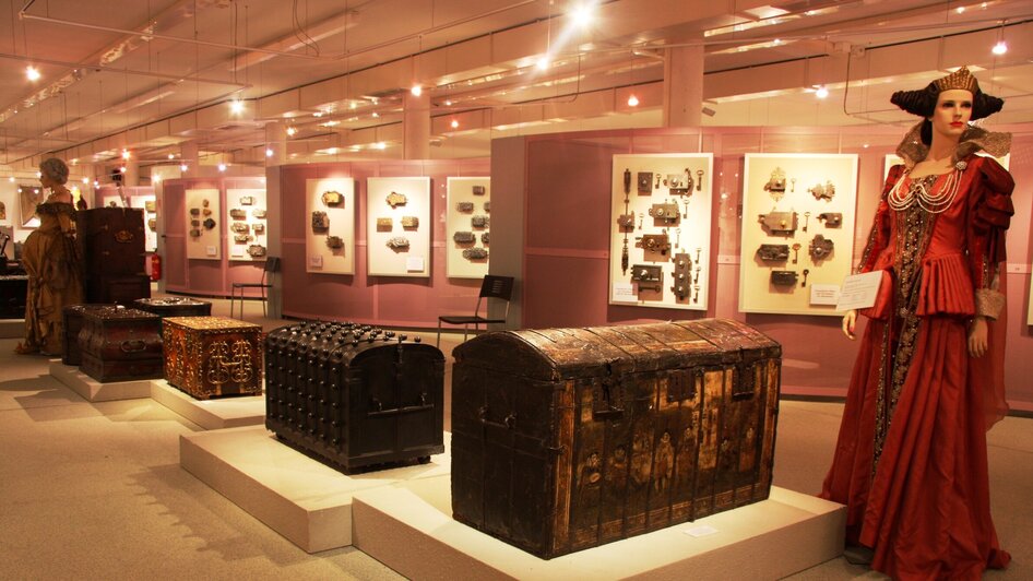 Historische Truhen und Kostüme in einer Ausstellung.