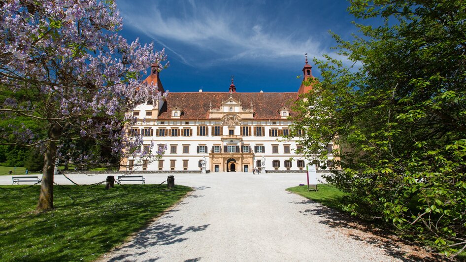 Schloss Eggenberg in Graz, umgeben von blühenden Bäumen und klarem Himmel. | © Graz Tourismus - Harry Schiffer