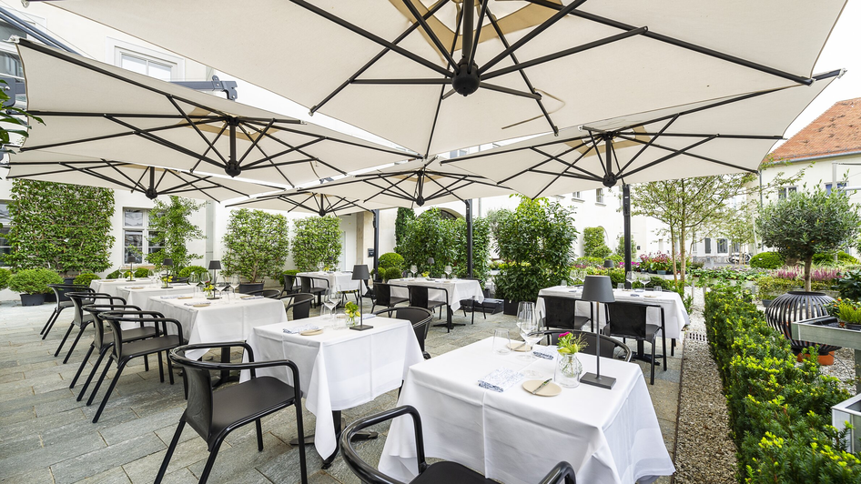 Gemütliche Terrasse mit weißen Tischen und Sonnenschirmen in Graz.